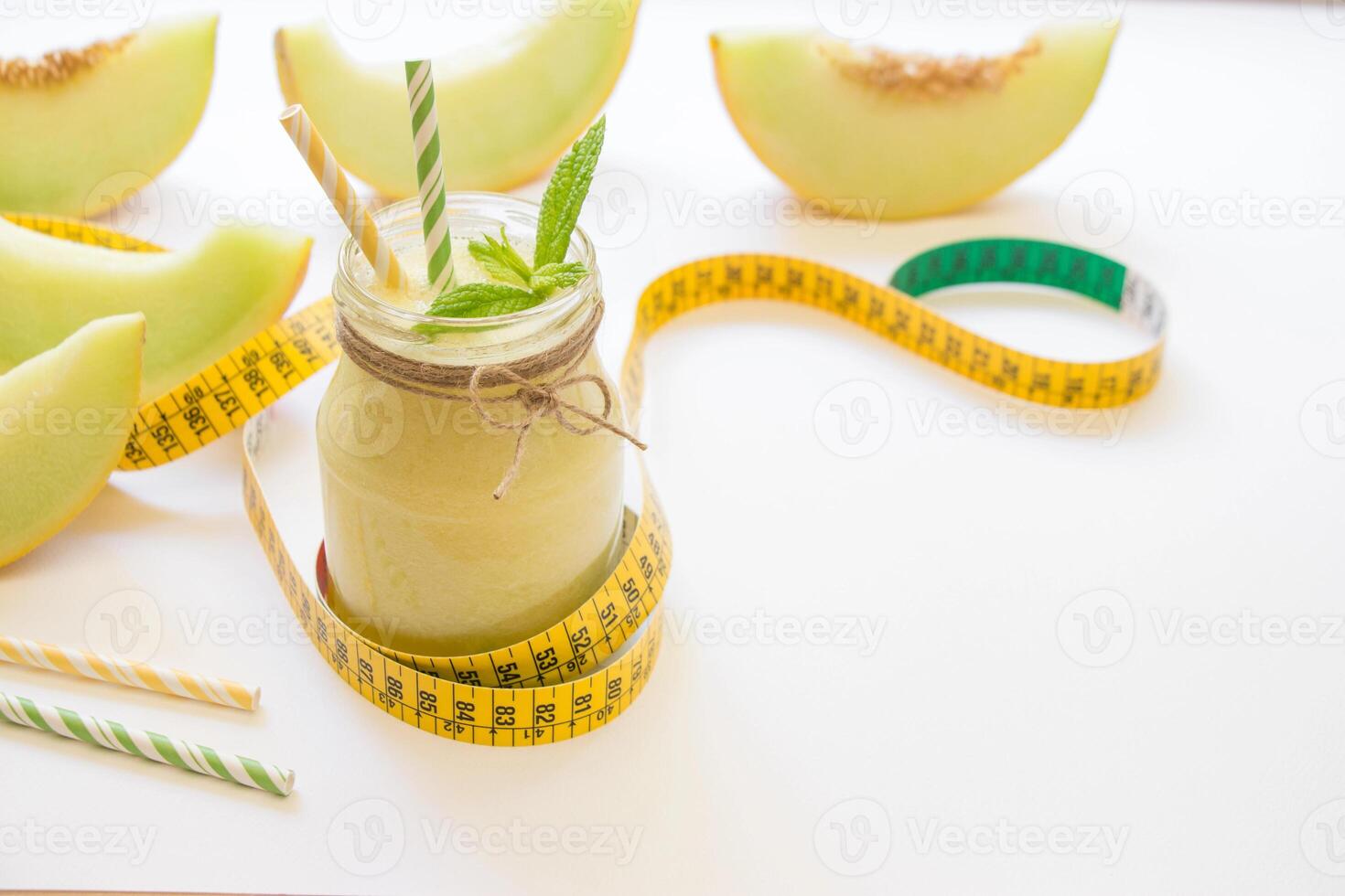 Left a jar with melon smoothie near cut slices of melon, centimeter, straws right empty place for text on a white background. Melon smoothie in a jar. Horizontal. Daylight. photo