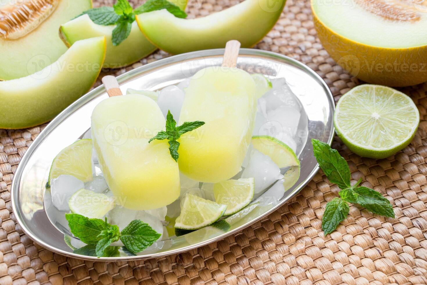 Enjoy refreshing melon ice cream popsicles presented on a silver tray surrounded by ice, mint, and lime, ideal for a warm afternoon gathering with friends or family. photo