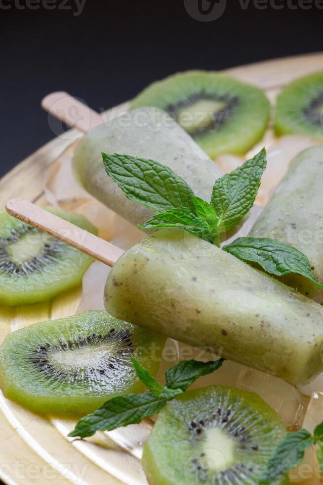 Kiwi ice cream popsicles are beautifully presented atop sliced kiwi fruits. Fresh mint leaves add a vibrant touch, enhancing the desserts visual appeal and flavor. photo