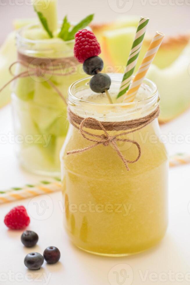 Two stylish jars filled with fruity drinks sit on a table, adorned with fresh raspberries, blueberries, and mint. Perfect for outdoor enjoyment. photo