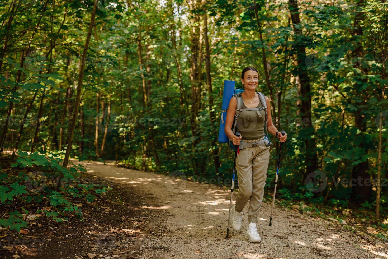 A woman enjoys trekking in a beautiful lush forest with a backpack and trekking poles photo