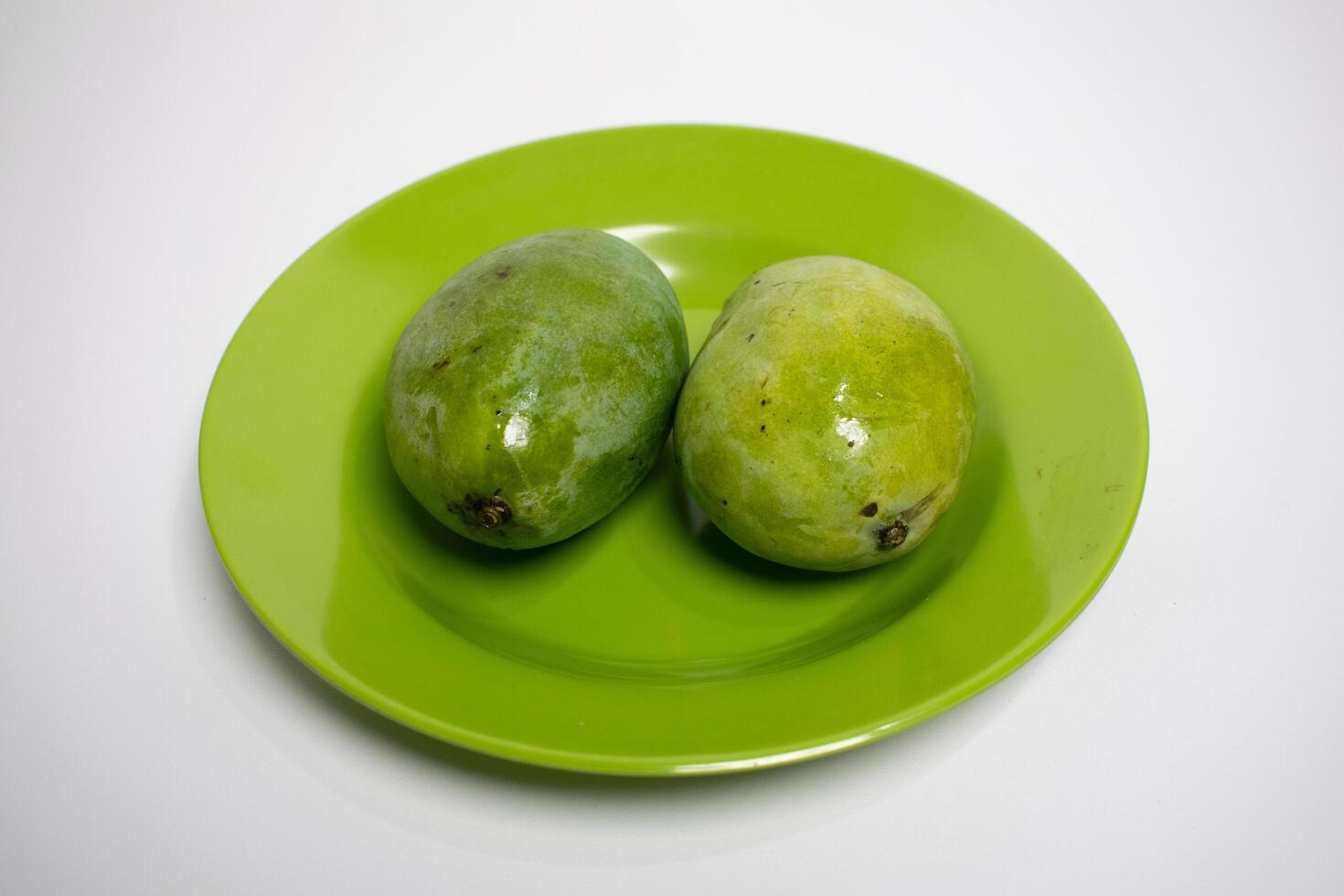 A pair of shiny green mangoes are placed side by side on a green plate. photo