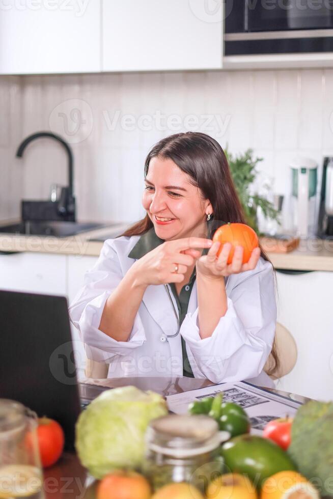 nutritionist conducting a consultation at a table with fruits and vegetables using a laptop and a tablet for notes. health concept, medical services. photo