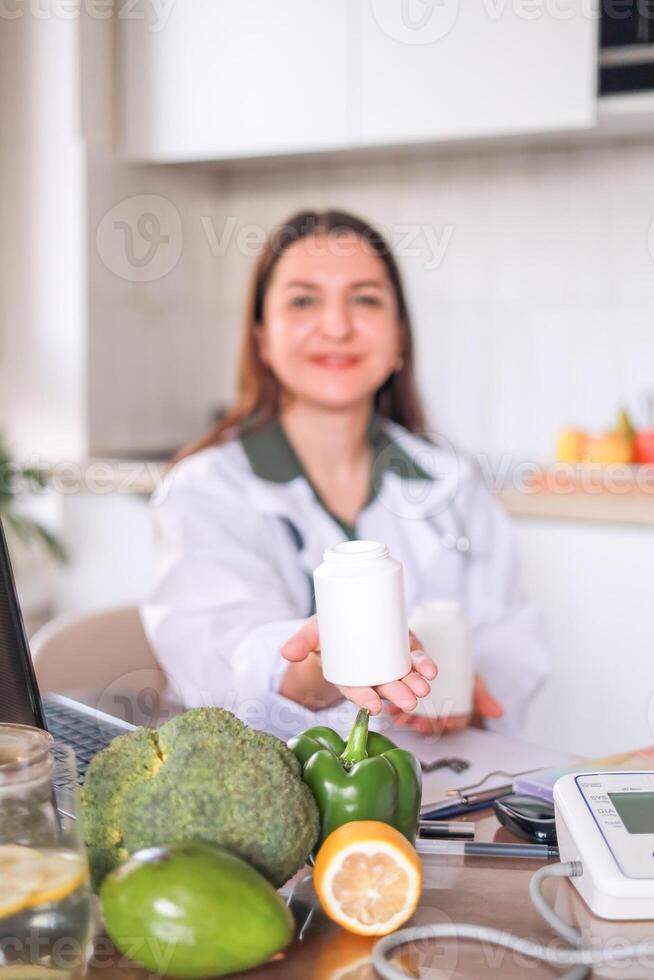 Dietitian in a white coat holds jars of dietary supplements and provides nutritional advice against the background of fresh vegetables and fruits. Curcumin, coenzyme q10. Health, wellness concept. photo
