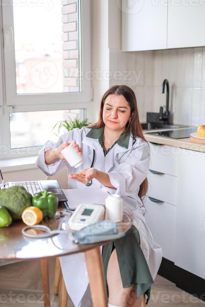A nutritionist pours pills and capsules of dietary supplements out of a jar and works at a table with healthy vegetables and fruits. Omega-3, B vitamins. Health, wellness concept. photo