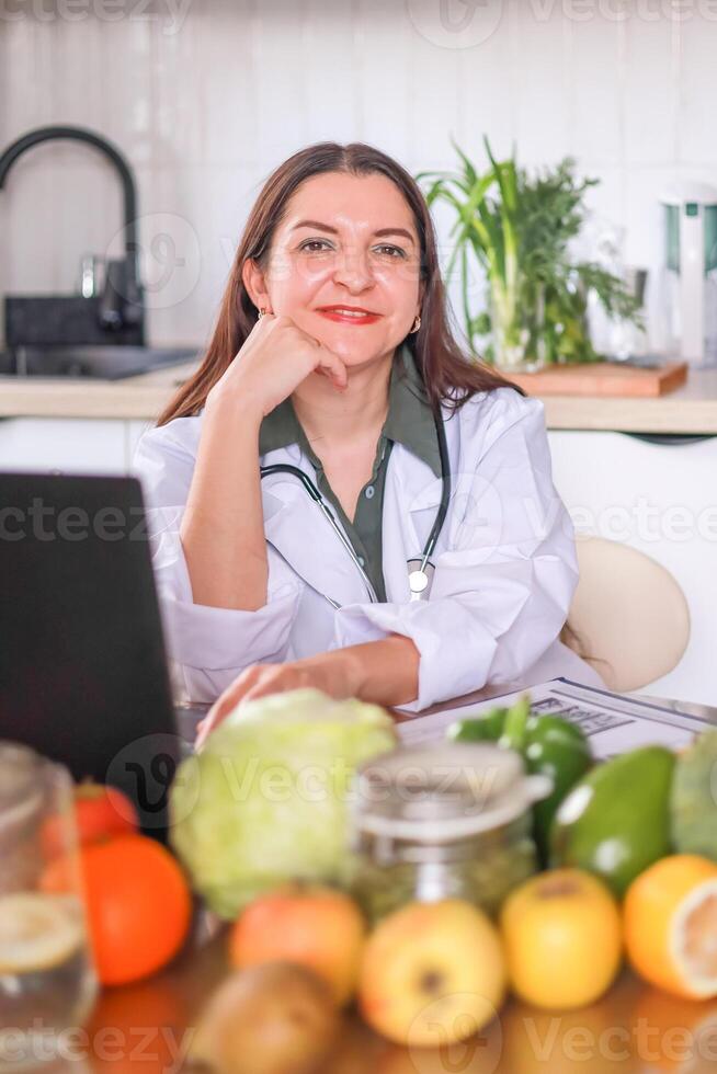 Close-up of a nutritionist at a table full of fresh vegetables and fruits using a laptop and a tablet to write down information. Health, wellness concept. photo