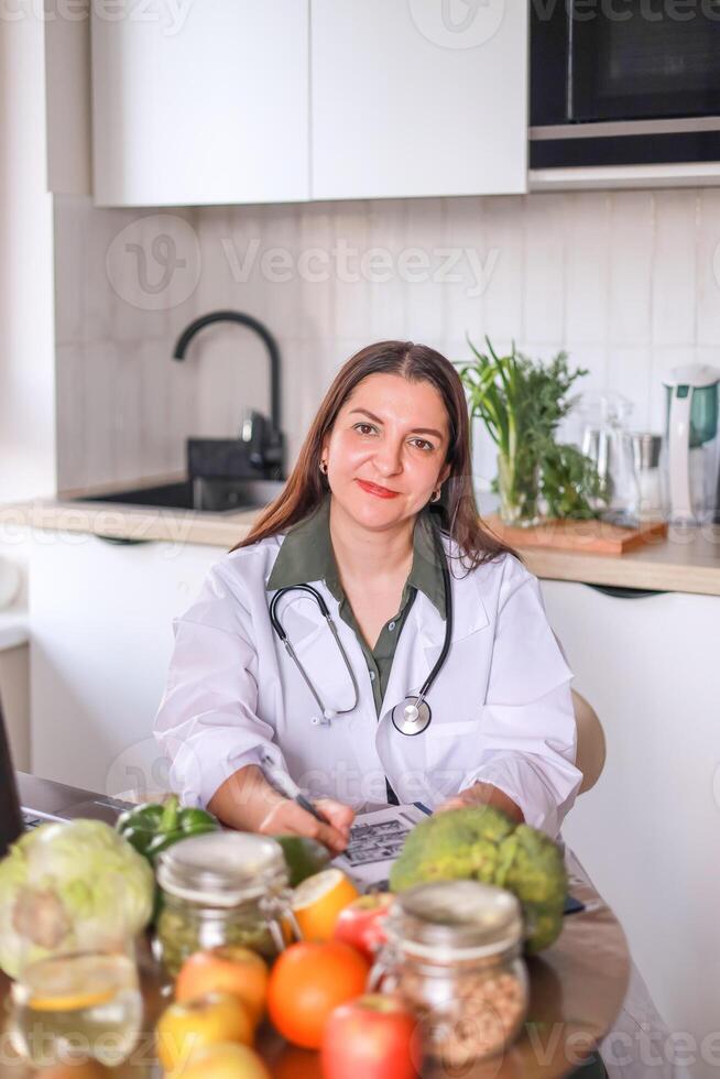 nutritionist in a white coat working at a table with fresh products and modern gadgets. nutrition concept, wellness programs. photo