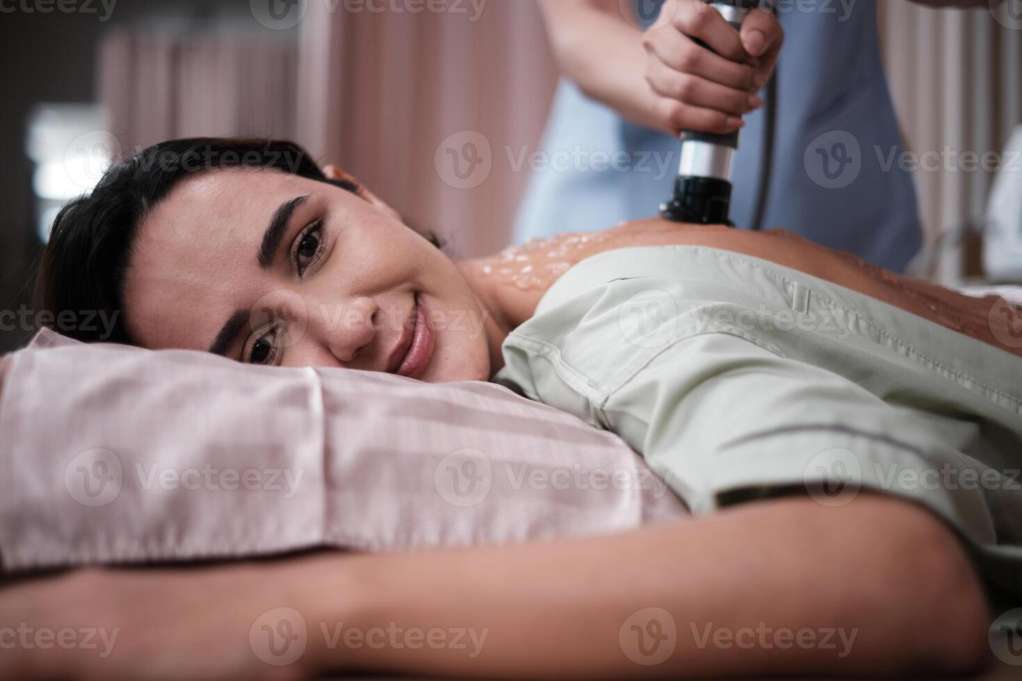 A female Latino patient recovered treated with ultrasound device for back pain relief procedure by Asian physical therapist, passive medical therapy at spa clinic, and wellness massaging healthcare. photo