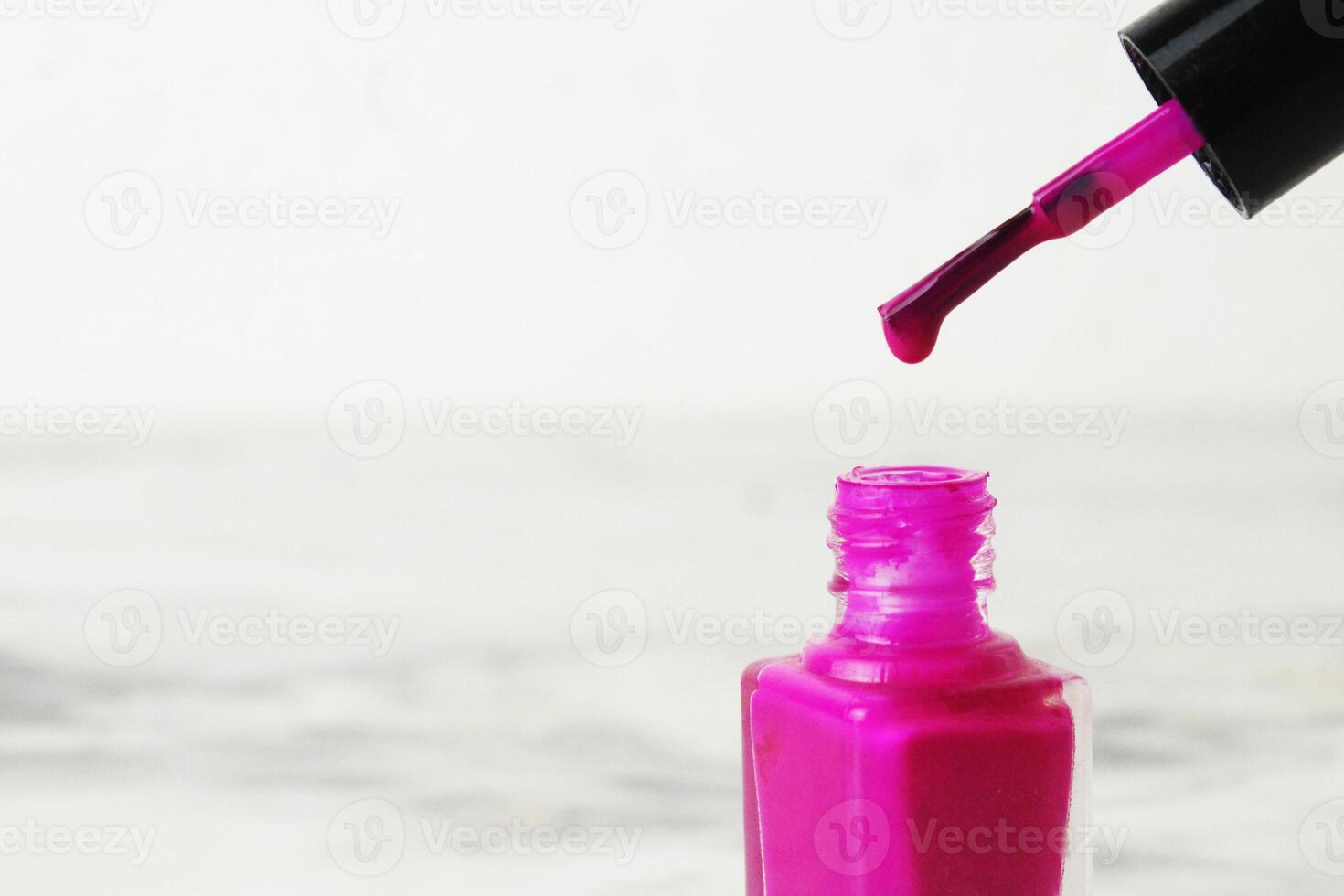 A drop of nail polish dripping from a brush close-up on a white background with space for copyspace text photo