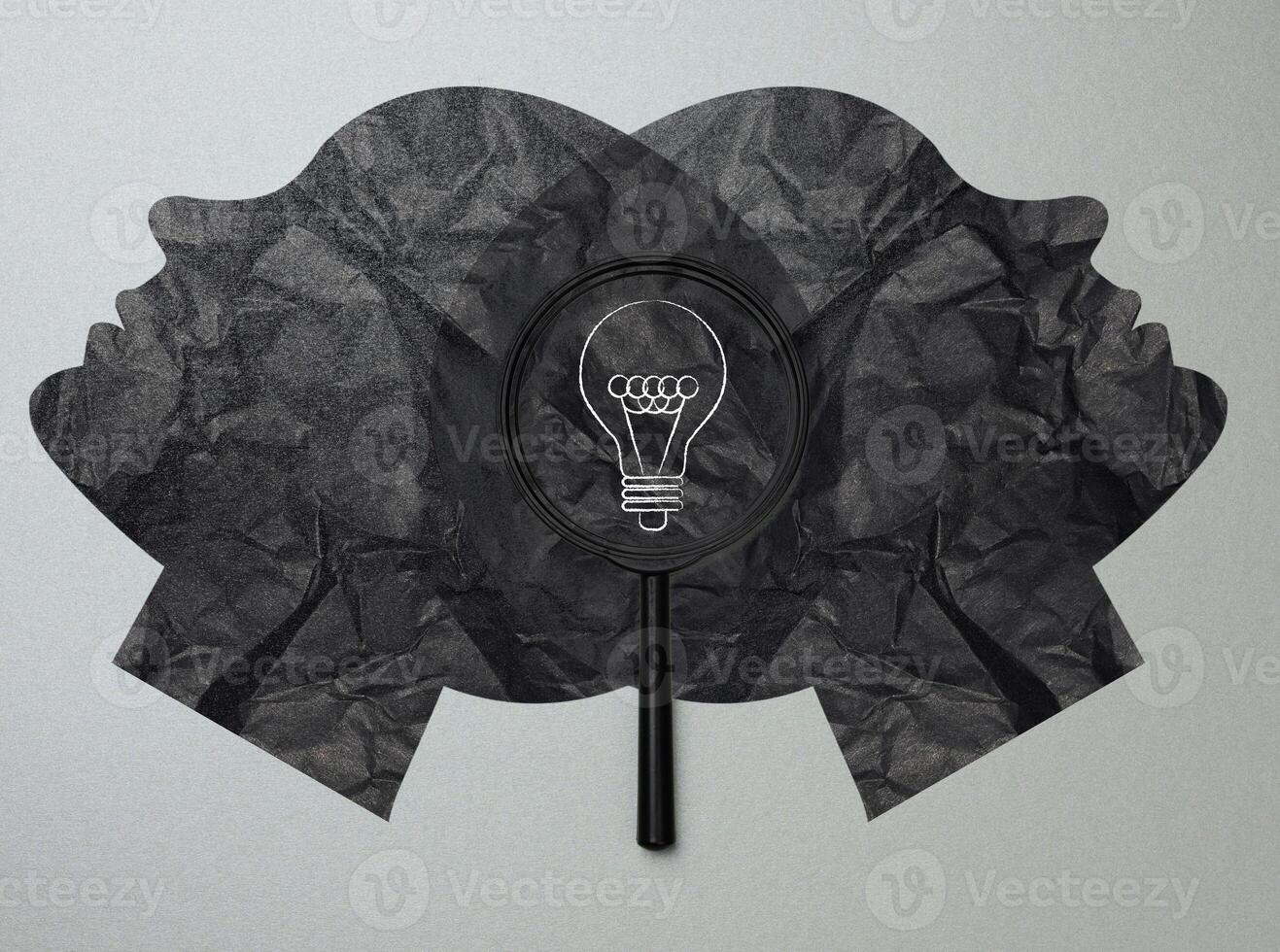 Two symmetrical black silhouettes of faces, in the center between them is a black magnifying glass, a light bulb painted in white photo