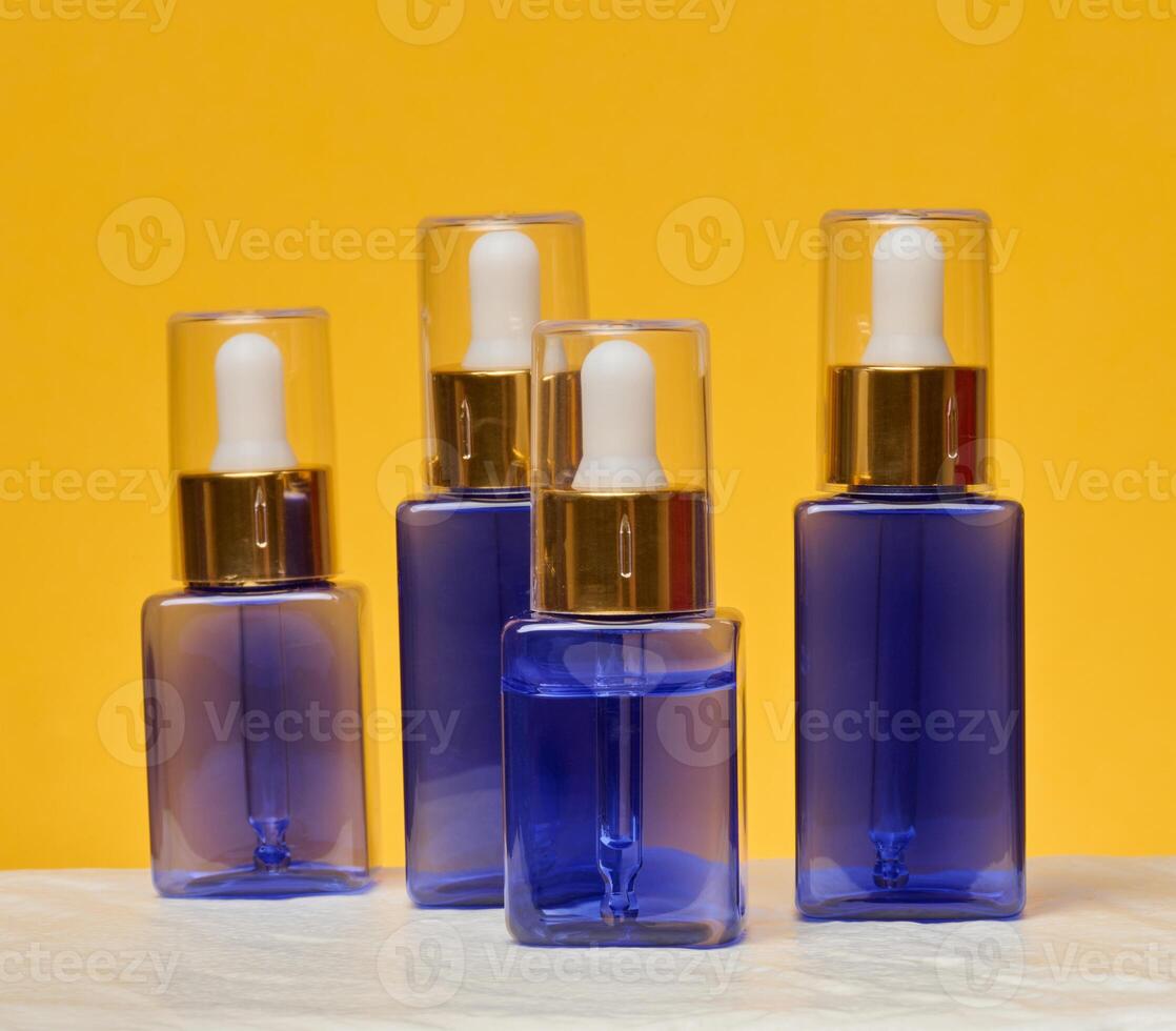 Transparent square blue bottles with gold caps and white pipettes photo