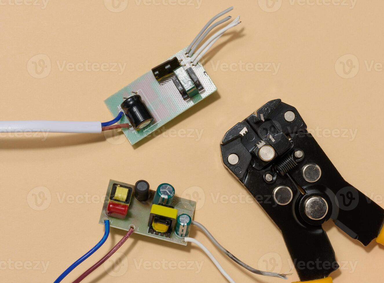 Two green electronic boards with components and wire stripper on beige background, top view. photo