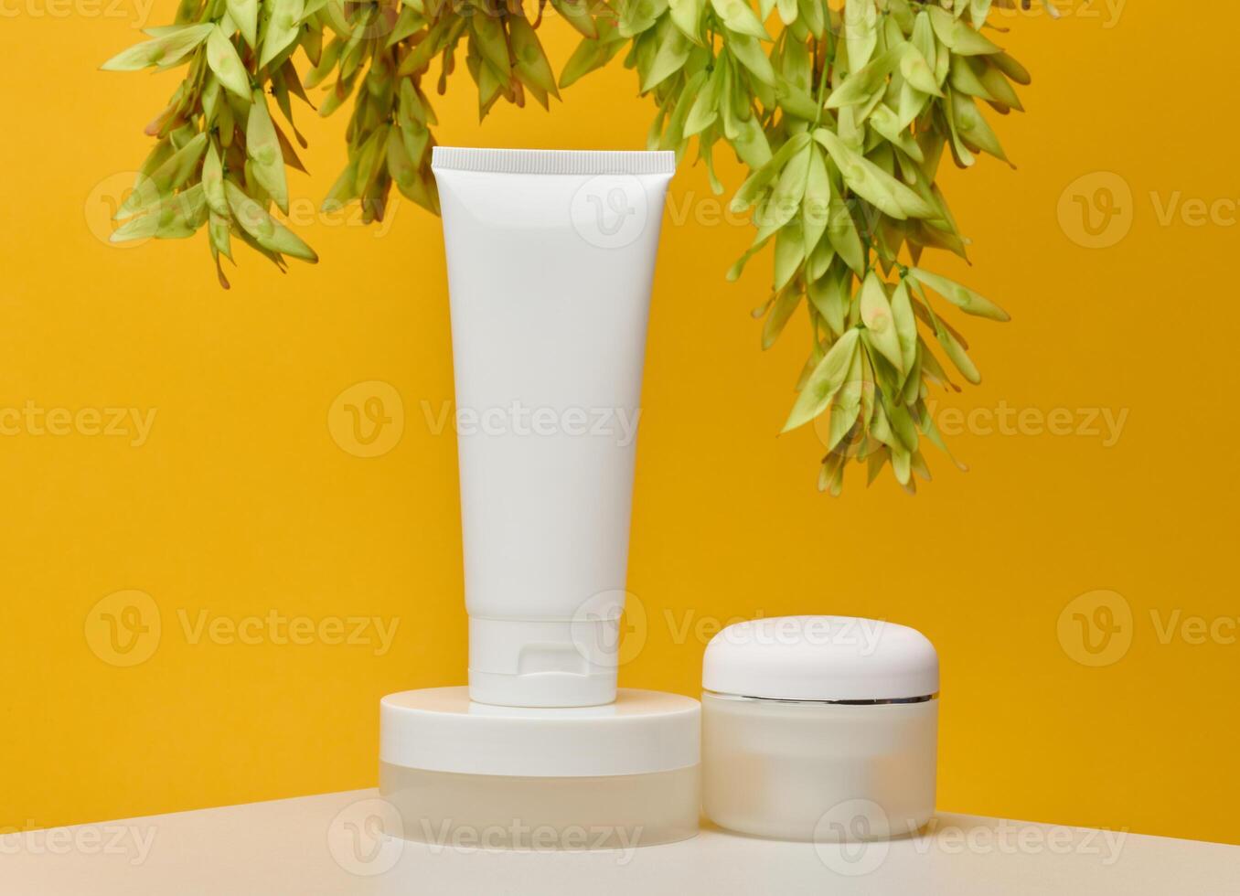 Three white cosmetic products without labels tube, flat round jar and short round jar, stand on white table against bright yellow background photo