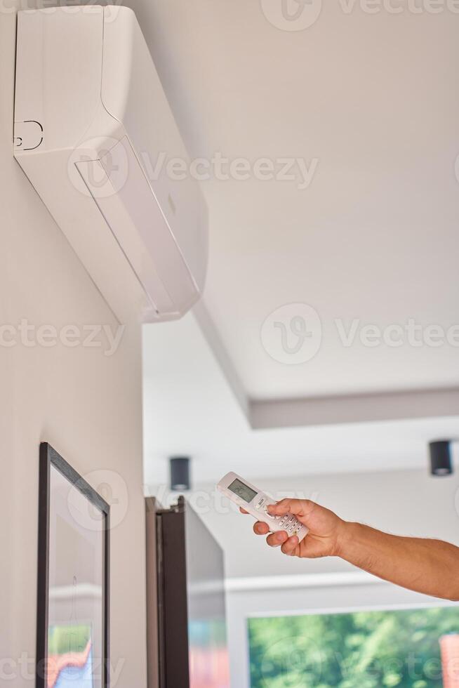 Hand using remote control to adjust temperature on air conditioner at home photo