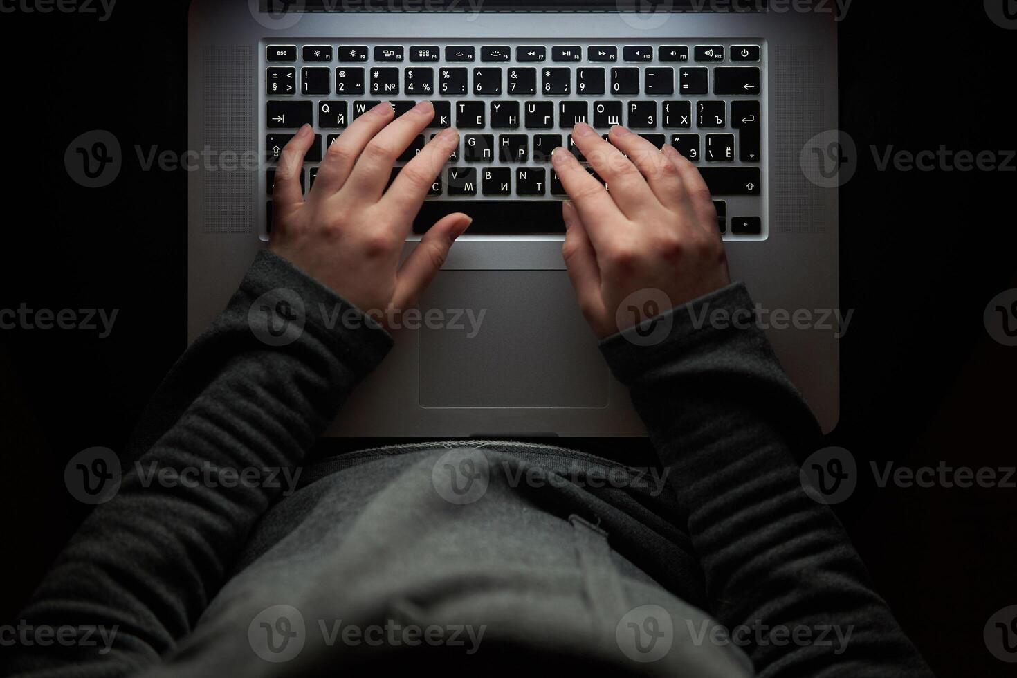 Overhead hacker in the hood working with laptop typing text in the darkroom. photo