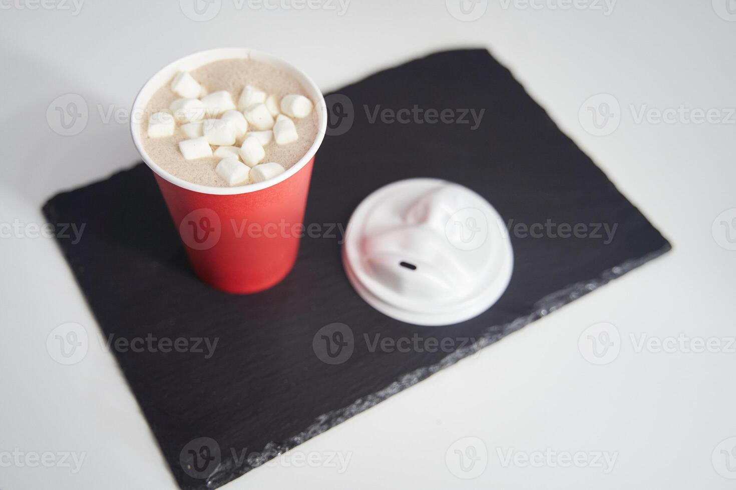 Red paper cup of coffee with marshmallows on a black tray. photo
