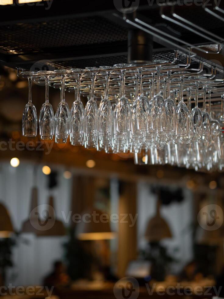 Row of clean glass in bar. Moody aesthetic image of bar and restaurant atmosphere with warm lightening and mane empty wine glasses. Row of clean polished wineglasses hanging in modern bar photo
