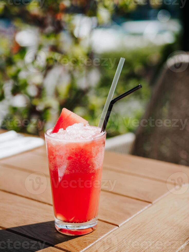 Fresh drink with watermelon, cold summer lemonade, healthy mocktail. Watermelon drink in sunny summer day shadows on wooden table background with copy space. Vertical. photo