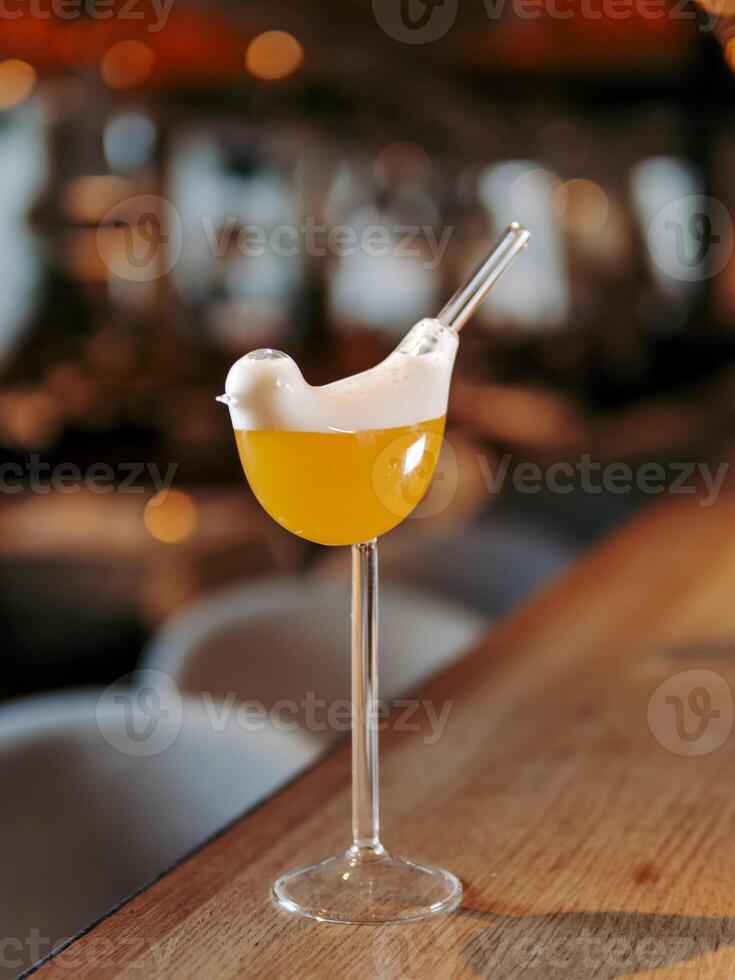 Tommy D Sour Cocktail in bird high stem cocktail glass on bar counter background with bokeh. Yellow alcohol Tommy Dee Sour cocktail made with whiskey, egg white, angostura, passion fruit syrup photo