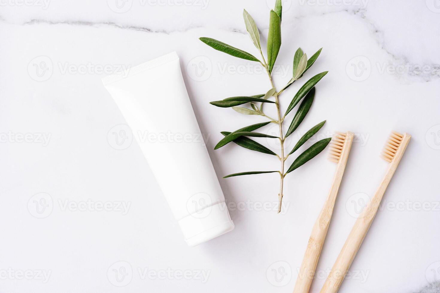 White plastic tube without label, bamboo toothbrushes and olive branch on white background photo