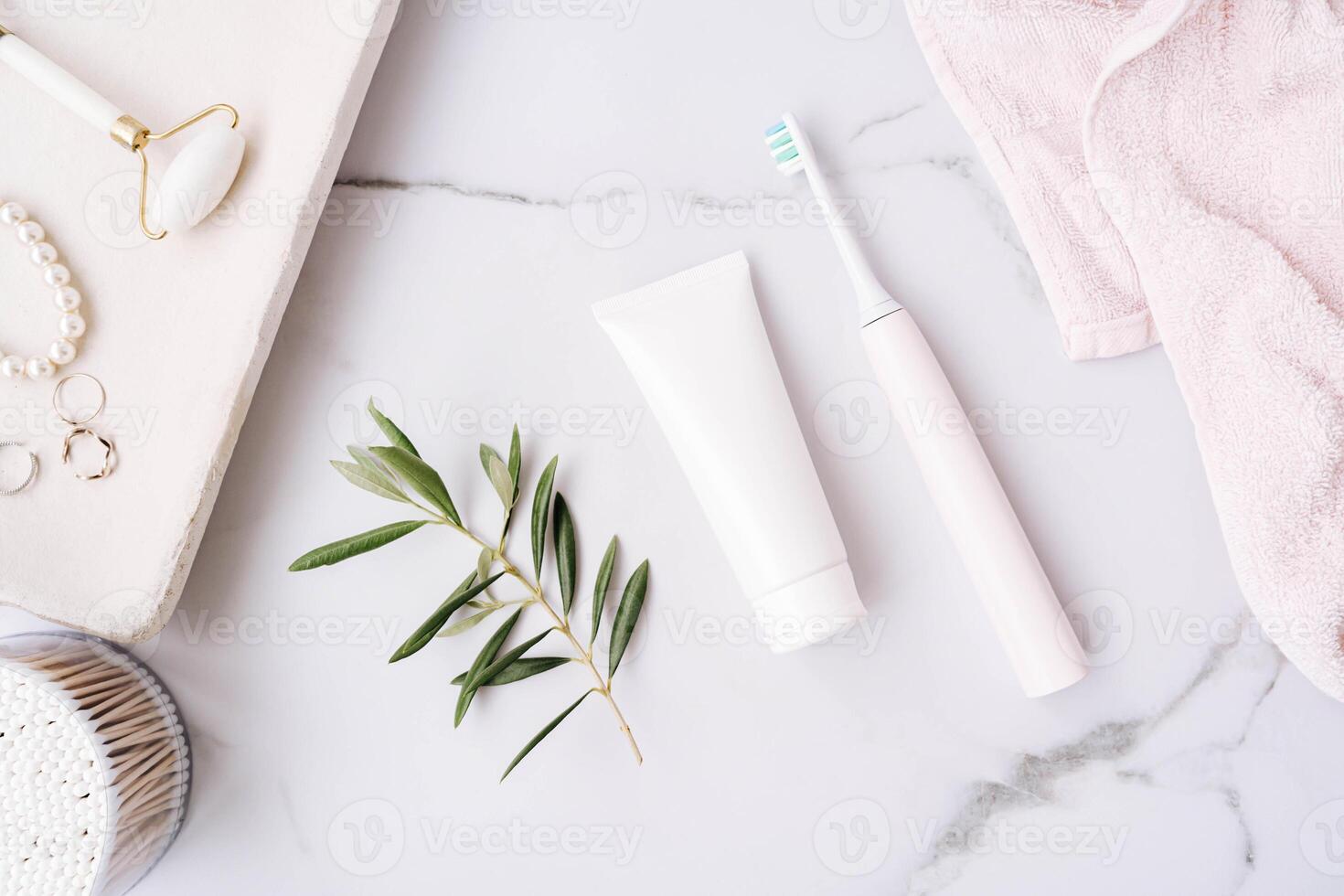 Top view of plastic tube without label, electric toothbrush and olive branch on white bath background photo