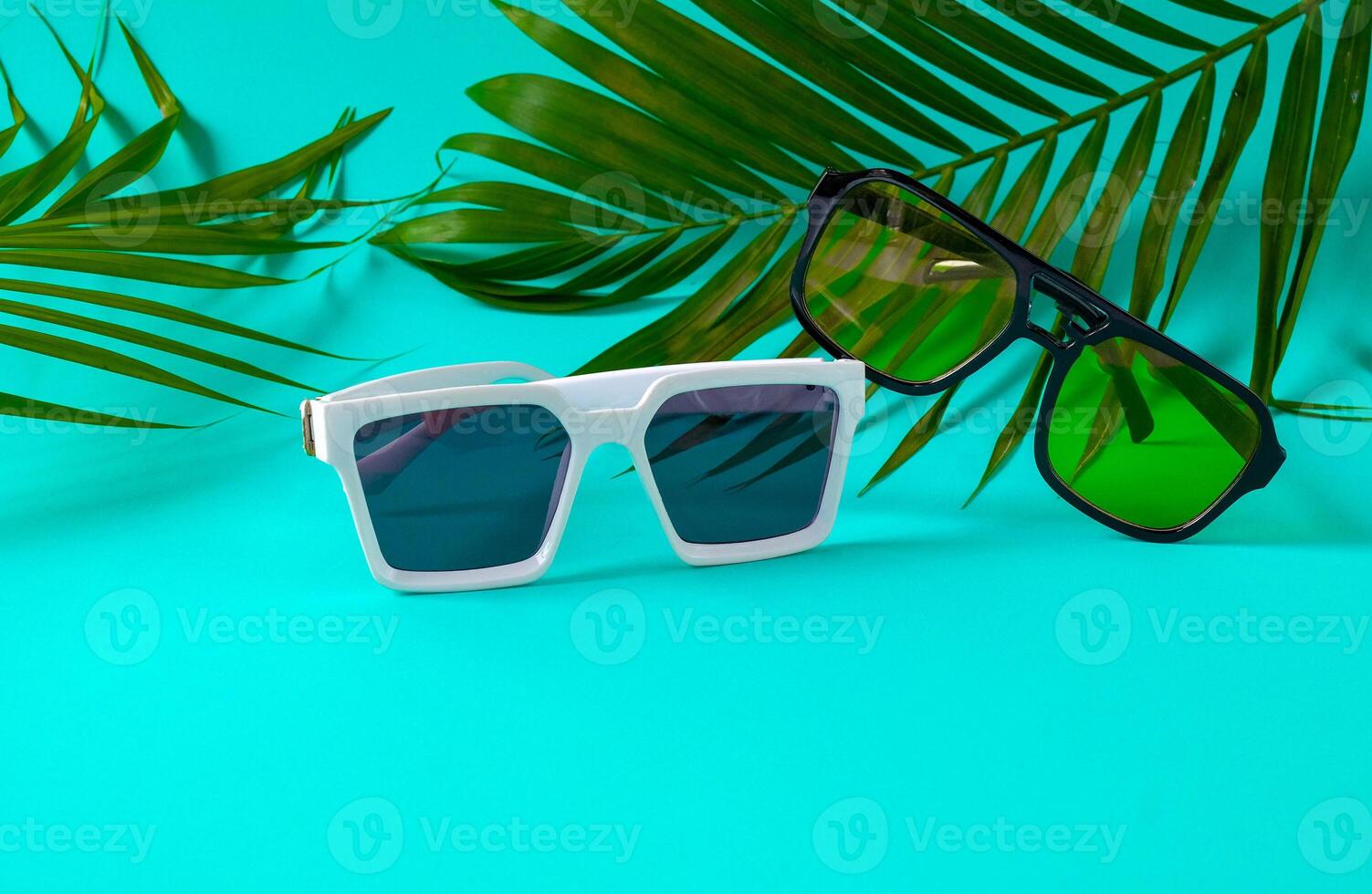 Trendy sunglasses on color wall with palm leaves. photo