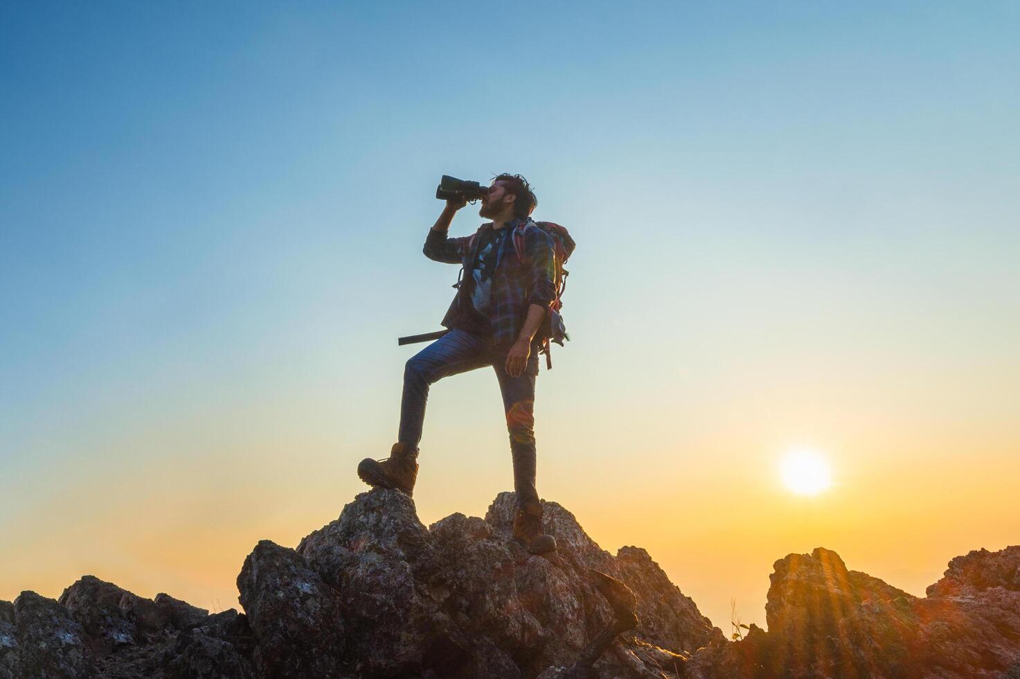 man is standing on a mountain top, looking through a camera lens photo