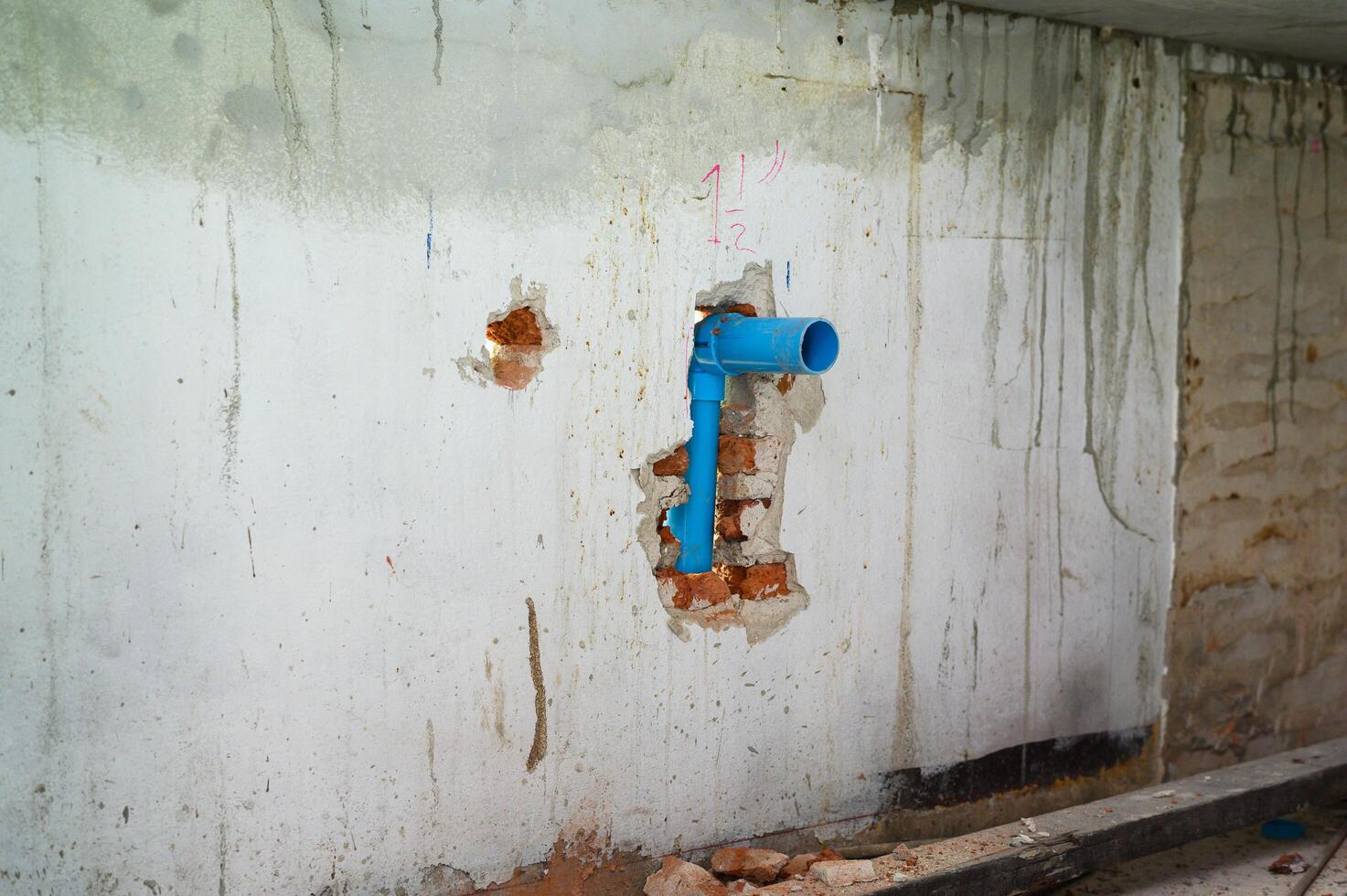 Old dirty concrete wall with broken blue pipe during house renovation. Grunge background showing plumbing repair and construction work with messy damage and decay photo
