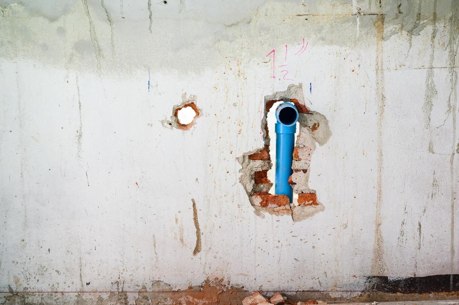 Damaged concrete wall with an exposed blue pipe in hole during major house renovation. Plumbing system work part of construction project with messy background view photo