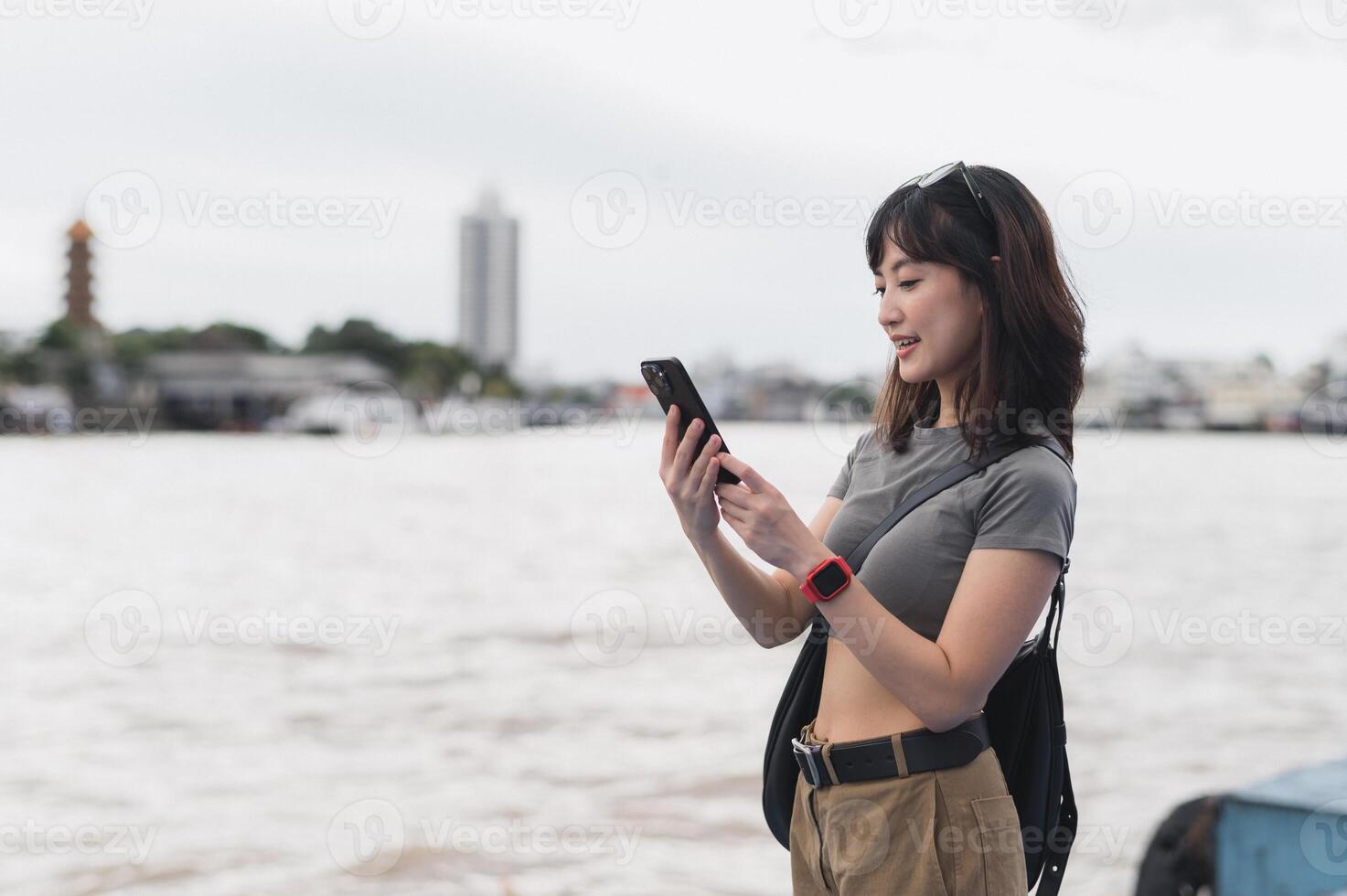 Happy solo southeast asian woman teenager blogger world travel tourism. Explorer wait for friend or express boat by Chao Phraya river. Local cultural experience smartphone concept Bangkok Thailand photo