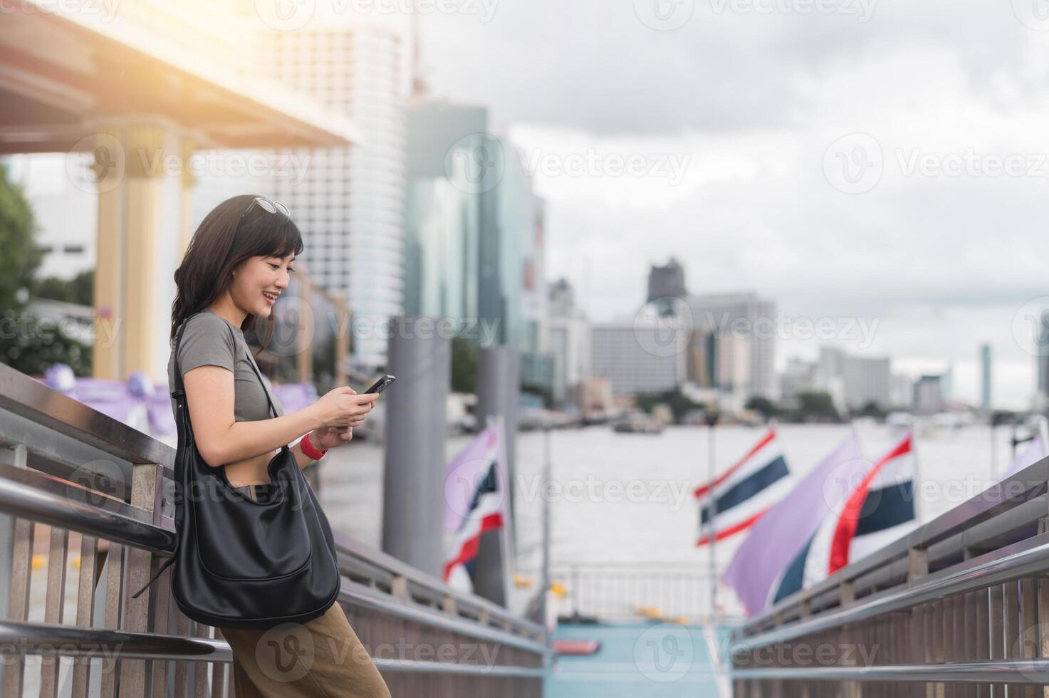 Happy young southeast asian woman and blogger searching map on smartphone. travel explorer on local cultural tourism experience in Bangkok Thailand near Chao Phraya river in Asia photo