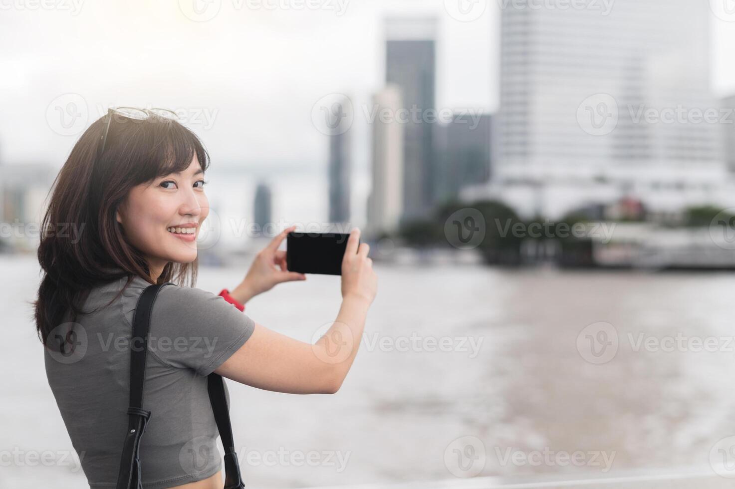 Happy solo asian woman on vacation taking photo of Bangkok with smartphone. Smiling blogger enjoys tour on Chao Phraya River, popular tourism concept for world travel explorer