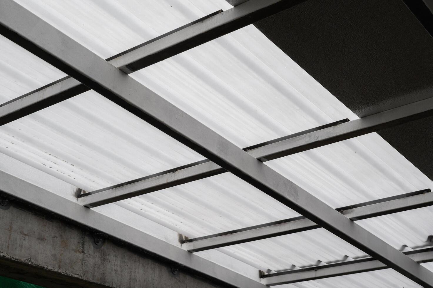 Metal beams supporting translucent sheet roofing. Light filters through corrugated sheet creating patterns. Strong metal framework provides stability shelter overhead. Durable sheet material photo