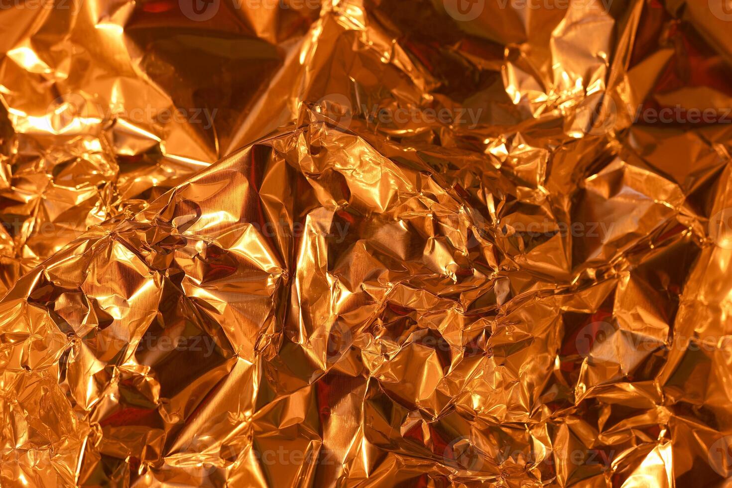Shimmering golden foil texture with intricate folds and crinkles reflecting light in warm tones photo