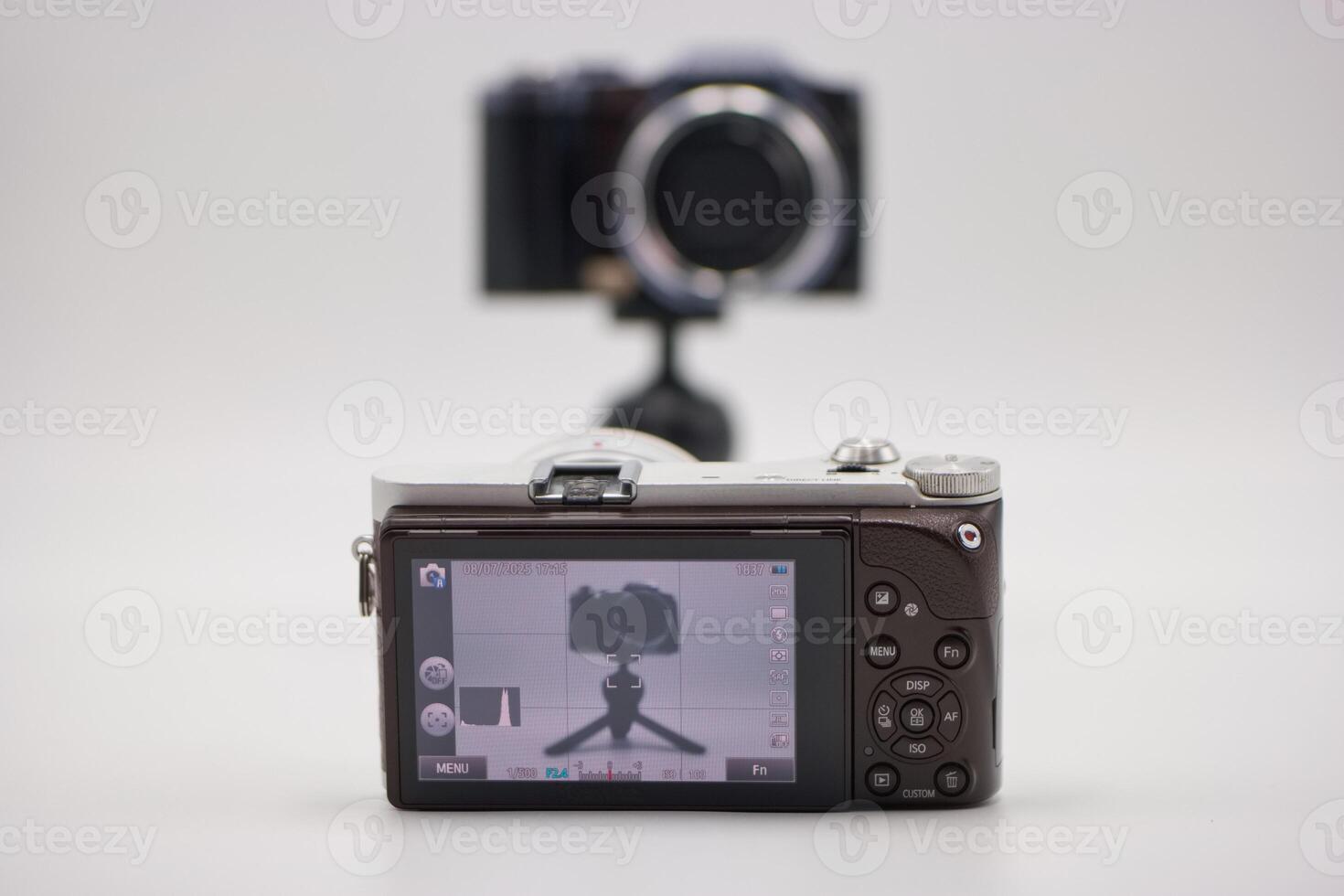 Camera setup on a tripod with a digital display showing reflection of another camera behind it photo