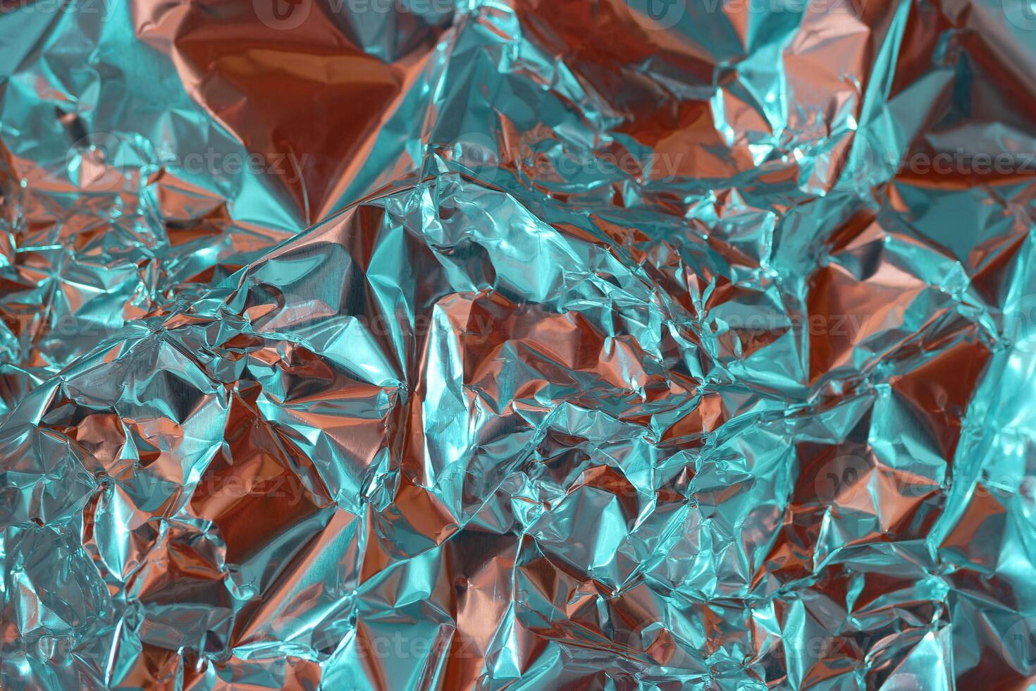 Shimmering crumpled foil creating an abstract texture with vibrant turquoise and orange hues in well lit surroundings photo