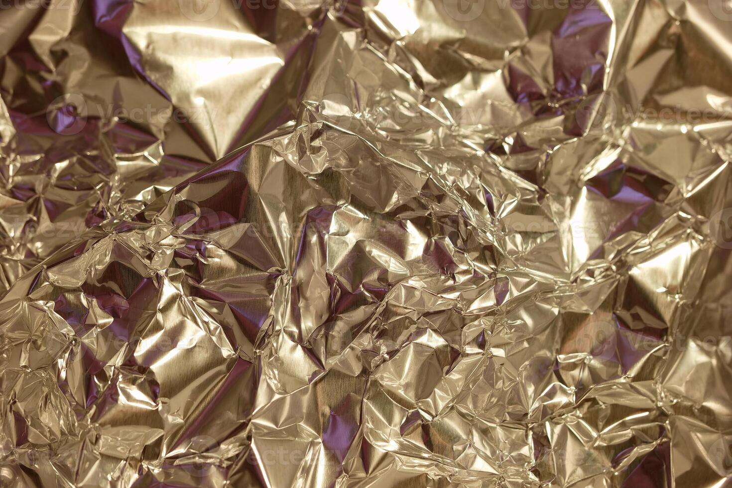 Shiny crumpled metallic foil in various shades reflecting light and creating interesting textures in a close up view photo