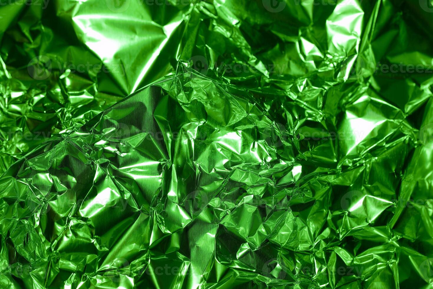 Crumpled green foil creating a textured surface with reflections and highlights visible under bright light photo