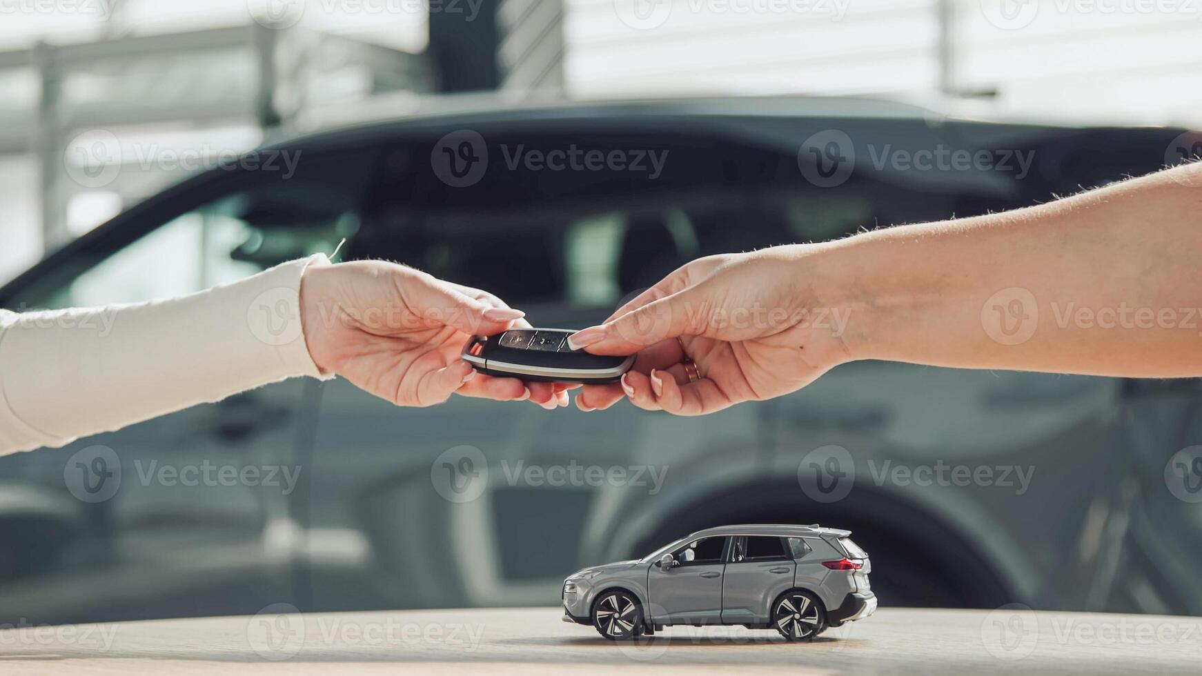 A toy small car drives across the table, and then the seller hands the keys to the buyer after the purchase. Close-up of hands. Finalizing the transaction, buying or leasing a new car. photo