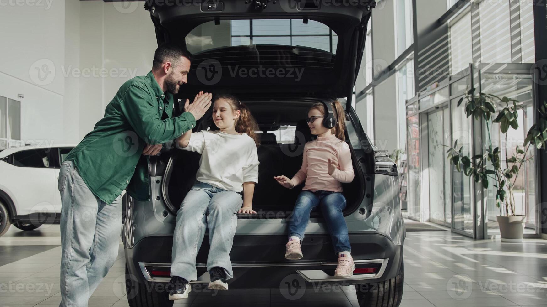 The end of a test drive or purchase of a new, modern car. A happy father with his two daughters sits in the trunk of the car he just bought. The happy family is enjoying the purchase. photo