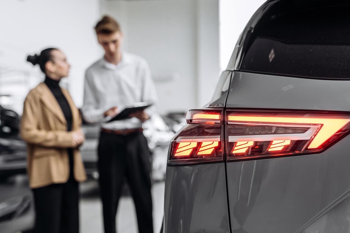 A car dealer in a modern car dealership advises a customer on buying or leasing a new car. The concept of an expensive purchase or lease of a modern car photo