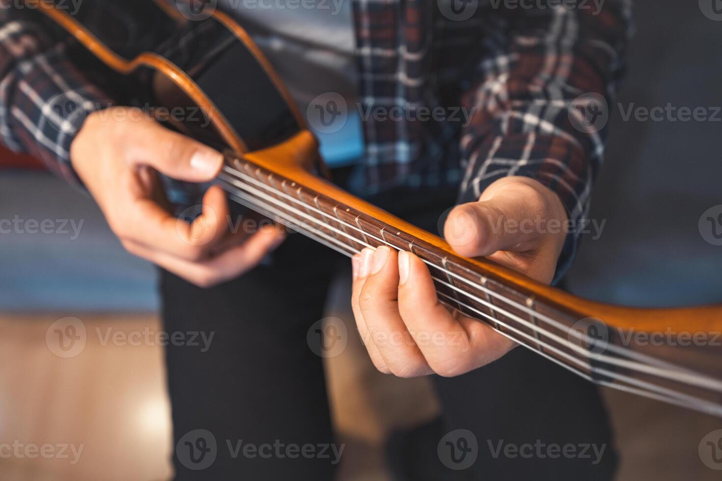 Smiling man gently presses chords on a classic ukulele while seated on a cozy couch. Home photo