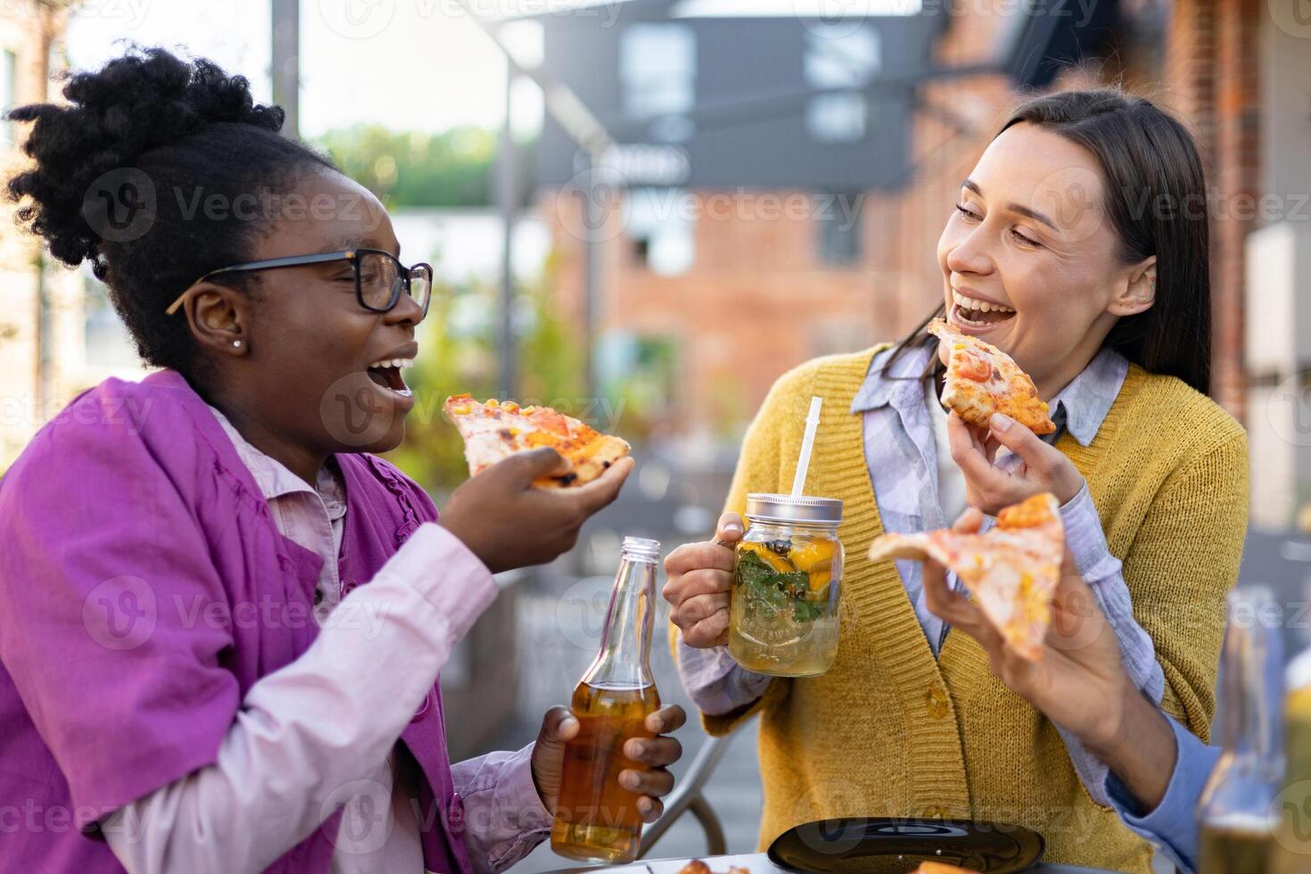 Two cheerful women share pizza and drinks outdoors, enjoying a relaxed meal together, laughing and having fun. photo