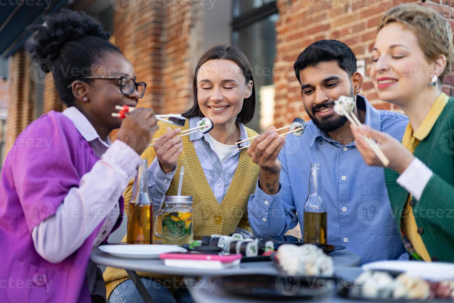 Diverse group of friends enjoying sushi and drinks outdoors, creating a relaxed and joyful dining experience. photo
