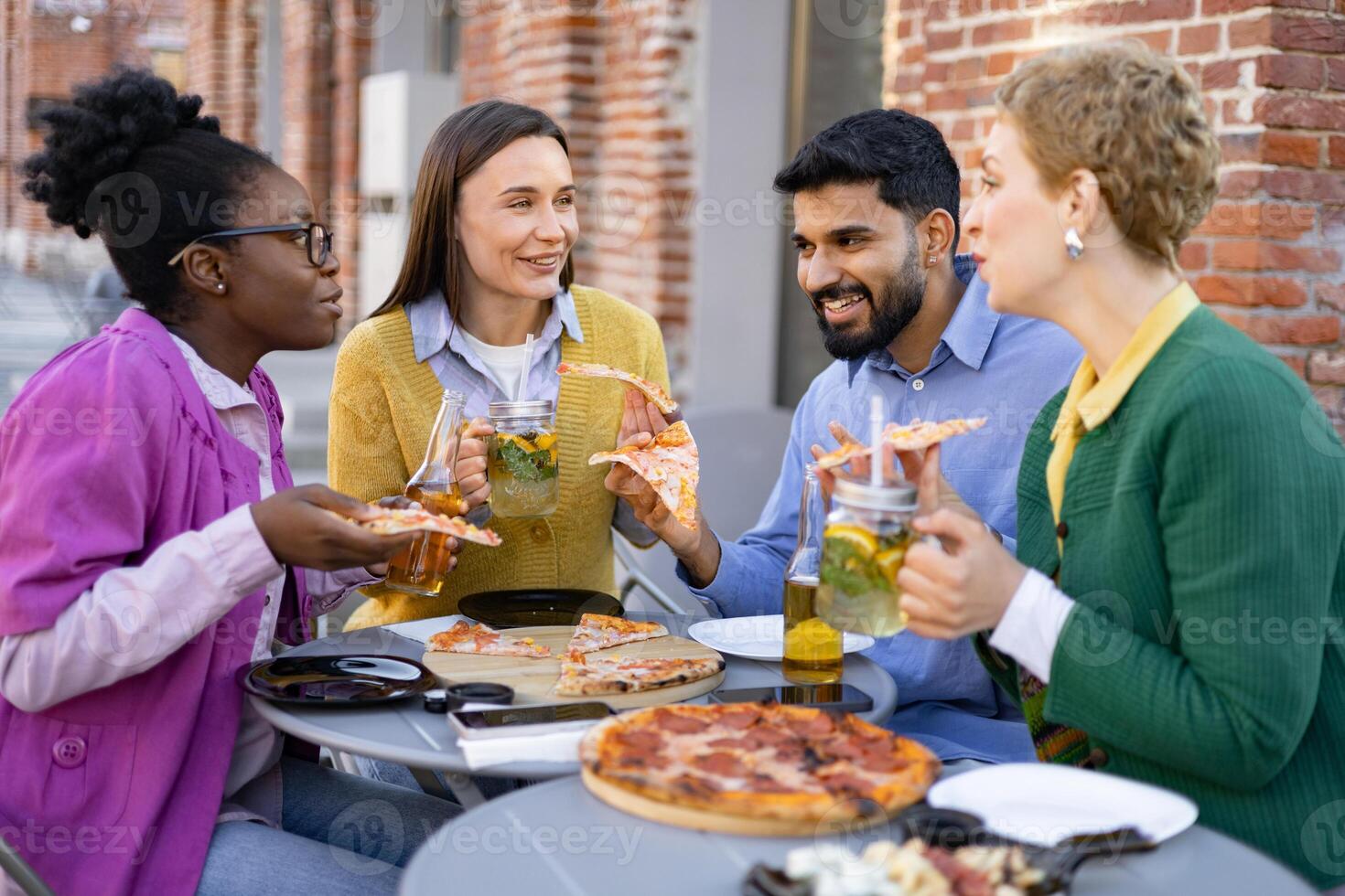 Diverse group of friends enjoying pizza and drinks outdoors, laughing and having a good time together. photo