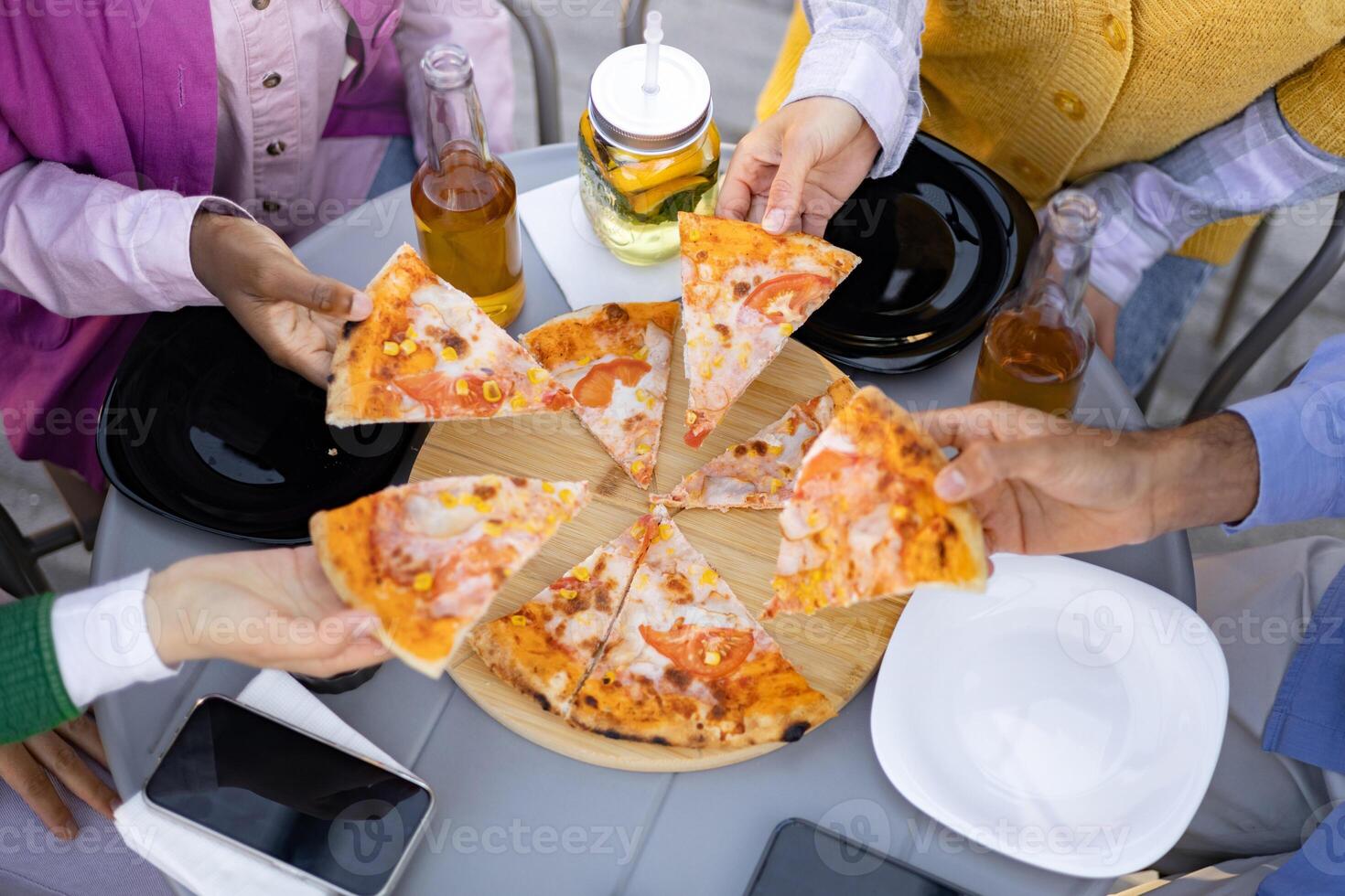 A group of friends enjoying pizza and drinks outdoors, capturing a moment of leisure and shared mealtime. photo