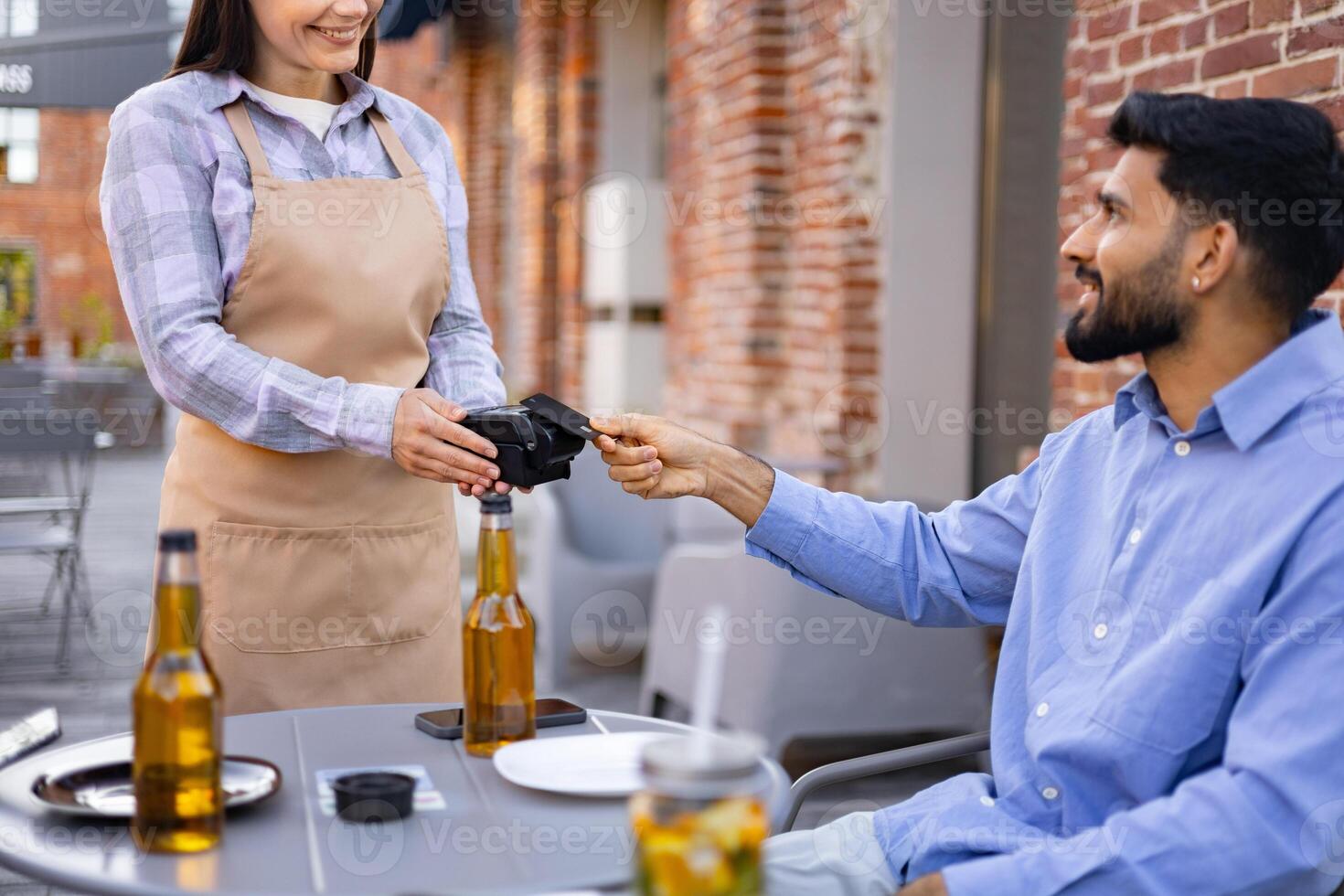 A smiling female waiter presents a payment terminal to a male customer seated at an outdoor cafe table. photo