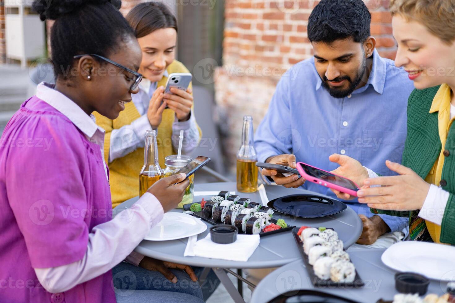 Friends gather for a sushi meal, each engrossed in their phones, creating a blend of social connection and digital engagement. photo