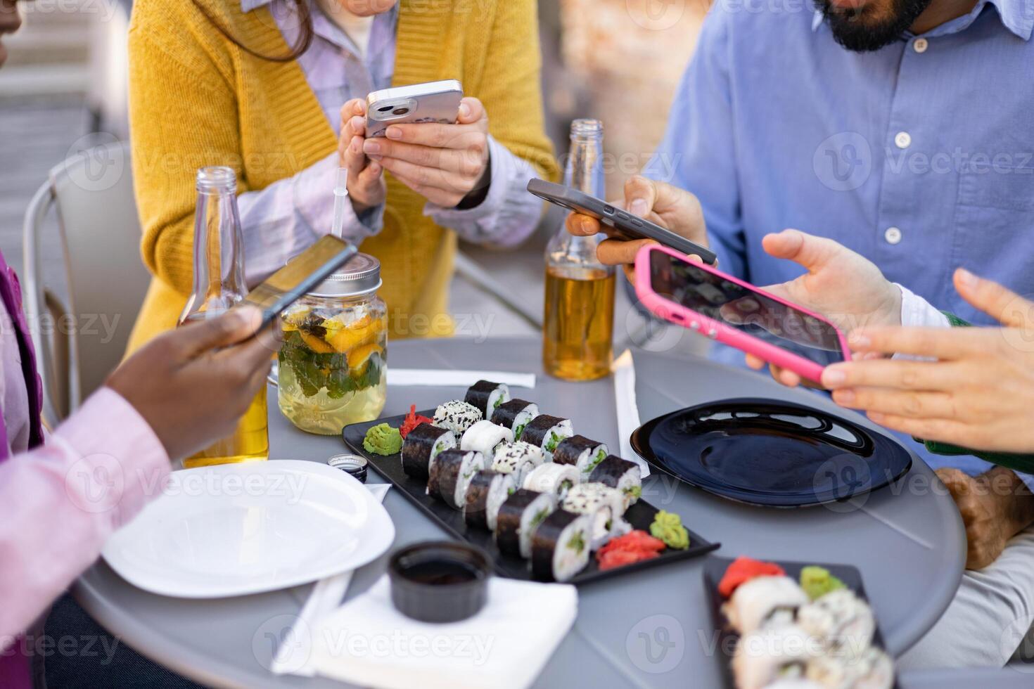 Friends enjoy sushi and drinks while using their phones at an outdoor gathering. photo