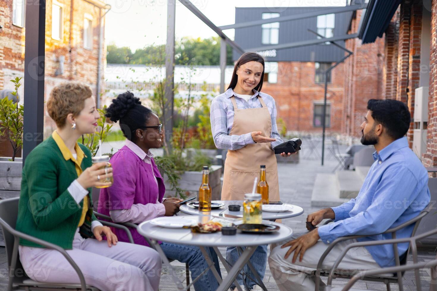 A female waiter presents a portable terminal to a customer, ready to process a payment at an outdoor cafe. photo